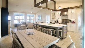 A spacious kitchen with a large island, wooden dining table, and wicker chairs. - Bayfront, Pool, Pier, 2 Hot Tubs!, Sandy Beach, Private, steps from beachfront (Saint George Island)