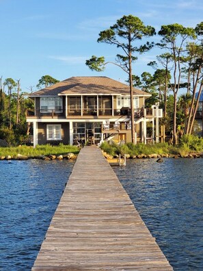 Una casa a due piani con un patio in legno che conduce all'ingresso, circondata dall'acqua e da alberi.