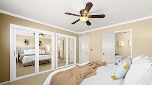 Ein Schlafzimmer mit Bett, Deckenventilator, Kleiderschrank und einem durch einen Spiegel sichtbaren Badezimmer.