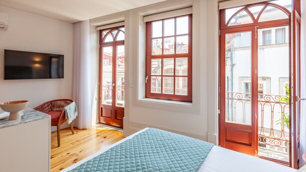 A bedroom with a bed, a TV, a chair, and a window with a view of buildings. - S. Bento Apart IV (G) (Oporto)