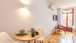 A dining area with a round table set for two, a TV mounted on the wall, and a wooden floor. - S. Bento Apart IV (G) (Oporto)