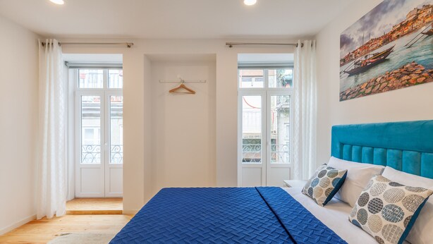 A bedroom with a bed, a blue headboard, and a painting of a coastal scene. - D&S - Villa Apartments & Suites II (Oporto)