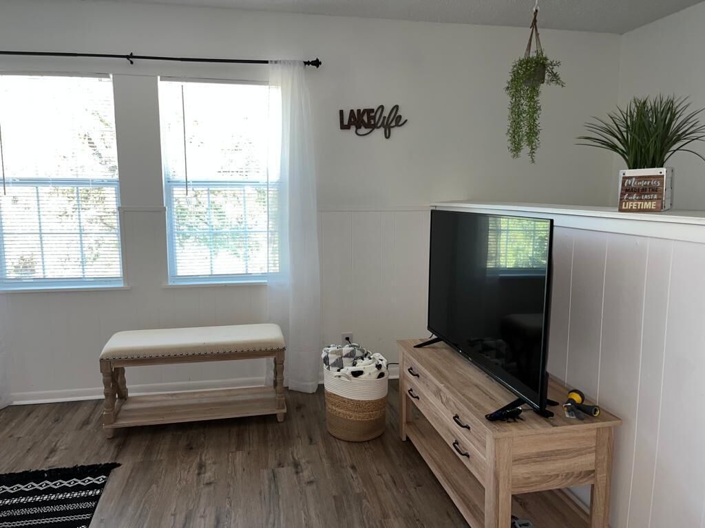 Een moderne woonkamer met een houten bank, een televisie op een houten dressoir, een mand en een bord met tekst op de muur.