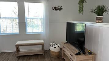 Een moderne woonkamer met een houten bank, een televisie op een houten dressoir, een mand en een bord met tekst op de muur.