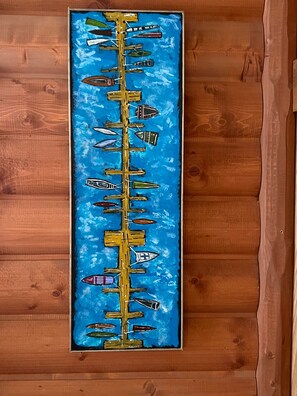 Pintura vertical que muestra varios barcos sobre un fondo azul, colgada en una pared de madera.