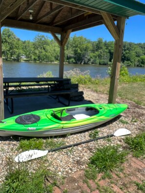 Un kayak verde, una mesa de picnic y un área techada junto a un lago.