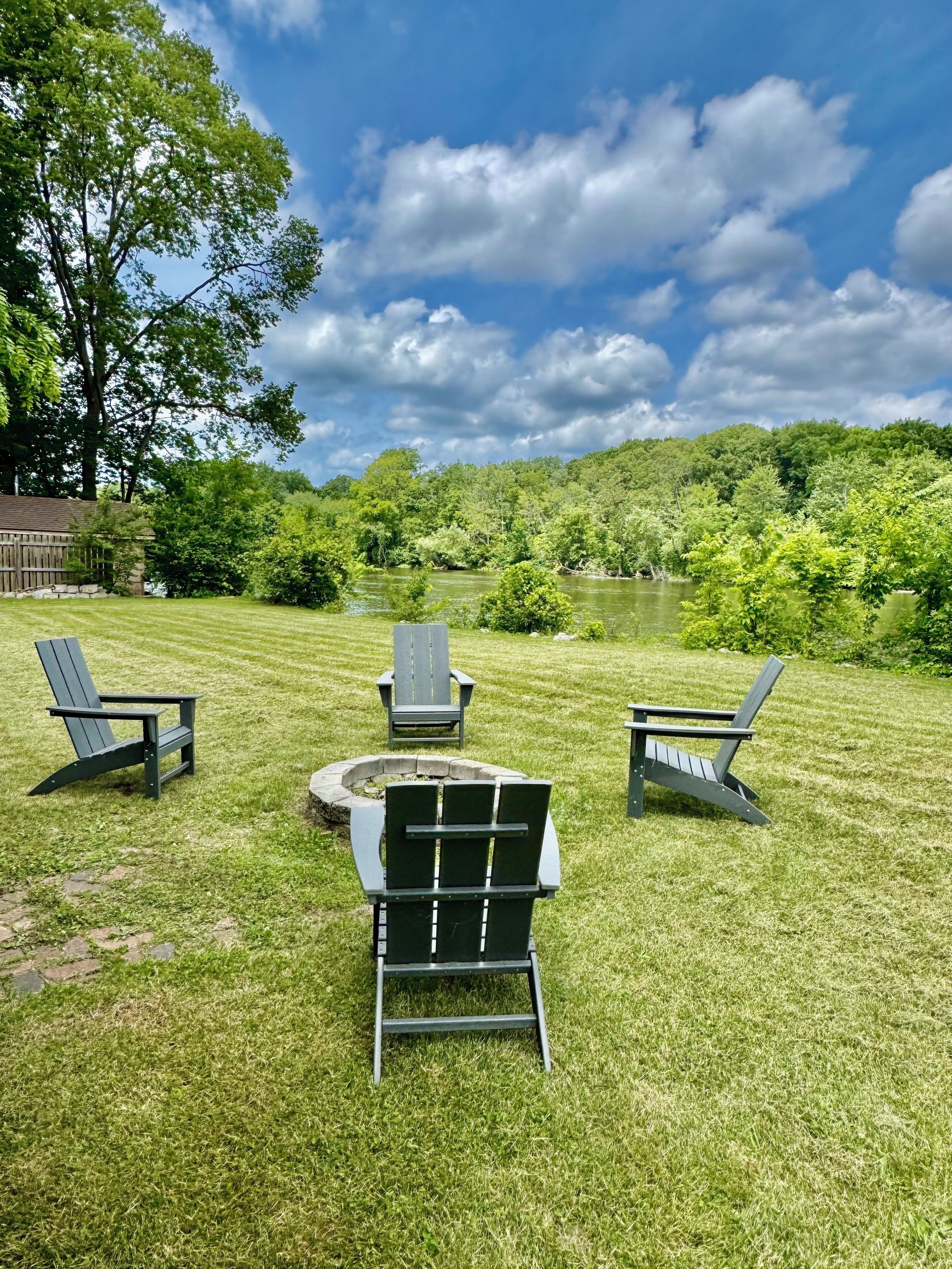 Un espace extérieur verdoyant avec trois fauteuils Adirondack et un foyer.