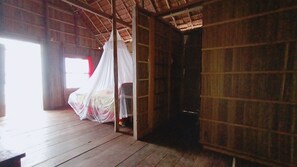 Ein Zimmer aus Holz mit einem Bett unter einem Moskitonetz, einer Holztür und einem Fenster mit roten Vorhängen.