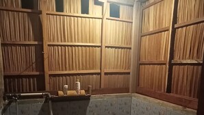 A small, dimly lit bathroom with wooden walls, a toilet, and a bucket. - Guest House (West Papua)