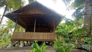 A wooden structure with a thatched roof, surrounded by palm trees and greenery. - Guest House (West Papua)