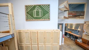A workshop with wooden cabinets, a green wall with a geometric design, and a loft area with a wooden ladder.
