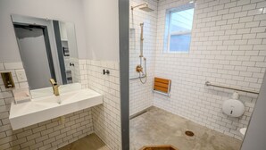 A bathroom with a white-tiled shower, a sink with a mirror, and a window.