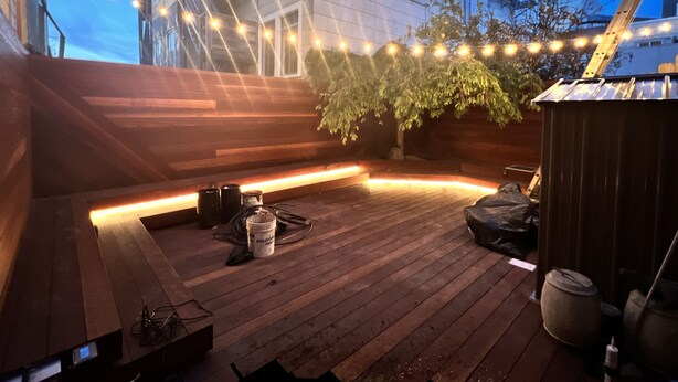 A wooden deck with string lights, a tree, and a building in the background.