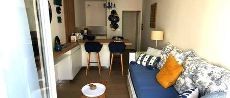 A compact living space with a kitchenette, a dining area, and a sofa with patterned cushions.