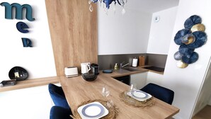 Una cocina moderna con encimera de madera, un fregadero y una máquina de café. Hay dos sillas y una mesa de comedor preparada con platos y vasos.