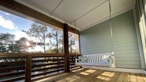 Une terrasse en bois avec un fauteuil suspendu et une vue sur les arbres et le ciel.