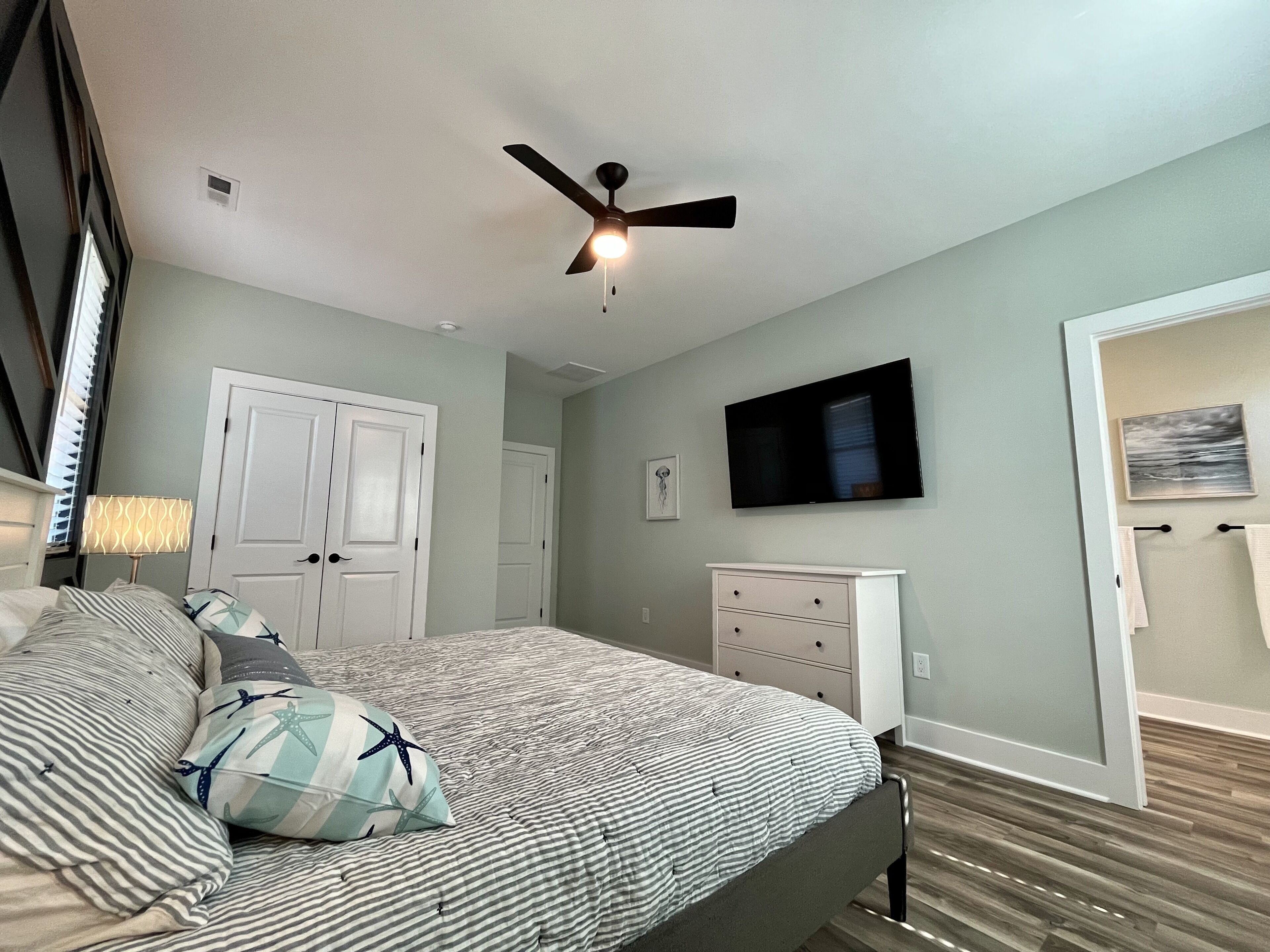 Ein Schlafzimmer mit Bett, Deckenventilator, Fernseher und Kommode.