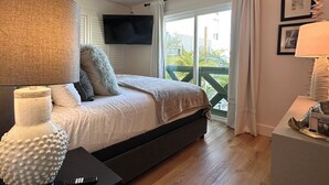 Een slaapkamer met een bed, een plafondventilator, een aan de muur bevestigde televisie en uitzicht op het landschap door een schuifdeur.