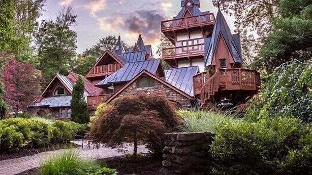 A rustic wooden house with multiple gabled roofs and a stone pathway leading to it.