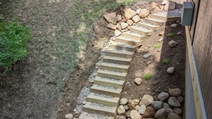 A wooden deck with a stone pathway leading to a grassy area.
