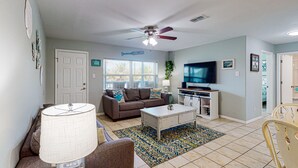 A living room with a ceiling fan, a television, a sofa, and a coffee table. - Shared Pool, Walk Path to Beach, golf Cart Access (Port Aransas)