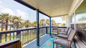 A covered outdoor area with a wooden deck, blue railing, and wicker furniture. - Shared Pool, Walk Path to Beach, golf Cart Access (Port Aransas)