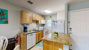A compact kitchen with wooden cabinets, a built-in dishwasher, a stove, and a refrigerator. - Shared Pool, Walk Path to Beach, golf Cart Access (Port Aransas)