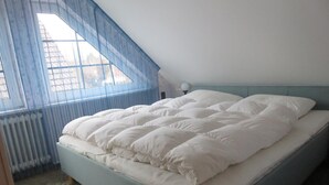 A bedroom with a bed, a window with blue curtains, a radiator, and a lamp on a bedside table.