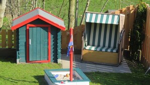 A small outdoor play area with a sandbox, a small shed, and a striped bench.