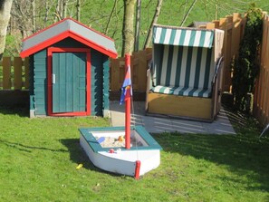 Een klein buitengebied met een zandbak, een tuinhuisje en een gestreepte bank.
