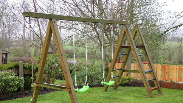 A wooden swing set with a ladder and a swing in a grassy backyard.