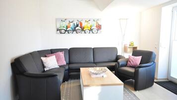Ein modernes Wohnzimmer mit einem schwarzen Ledersofa, einem weißen Couchtisch und einem farbenfrohen Kunstwerk mit Oldtimern an der Wand.
