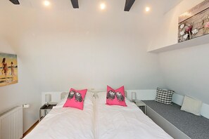 A bedroom with a large bed, two pillows with owl designs, a bedside table, a lamp, and a painting on the wall.