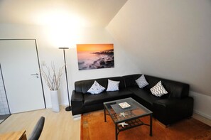 A modern living room with a black leather sofa, a glass coffee table, and a painting of a sunset.