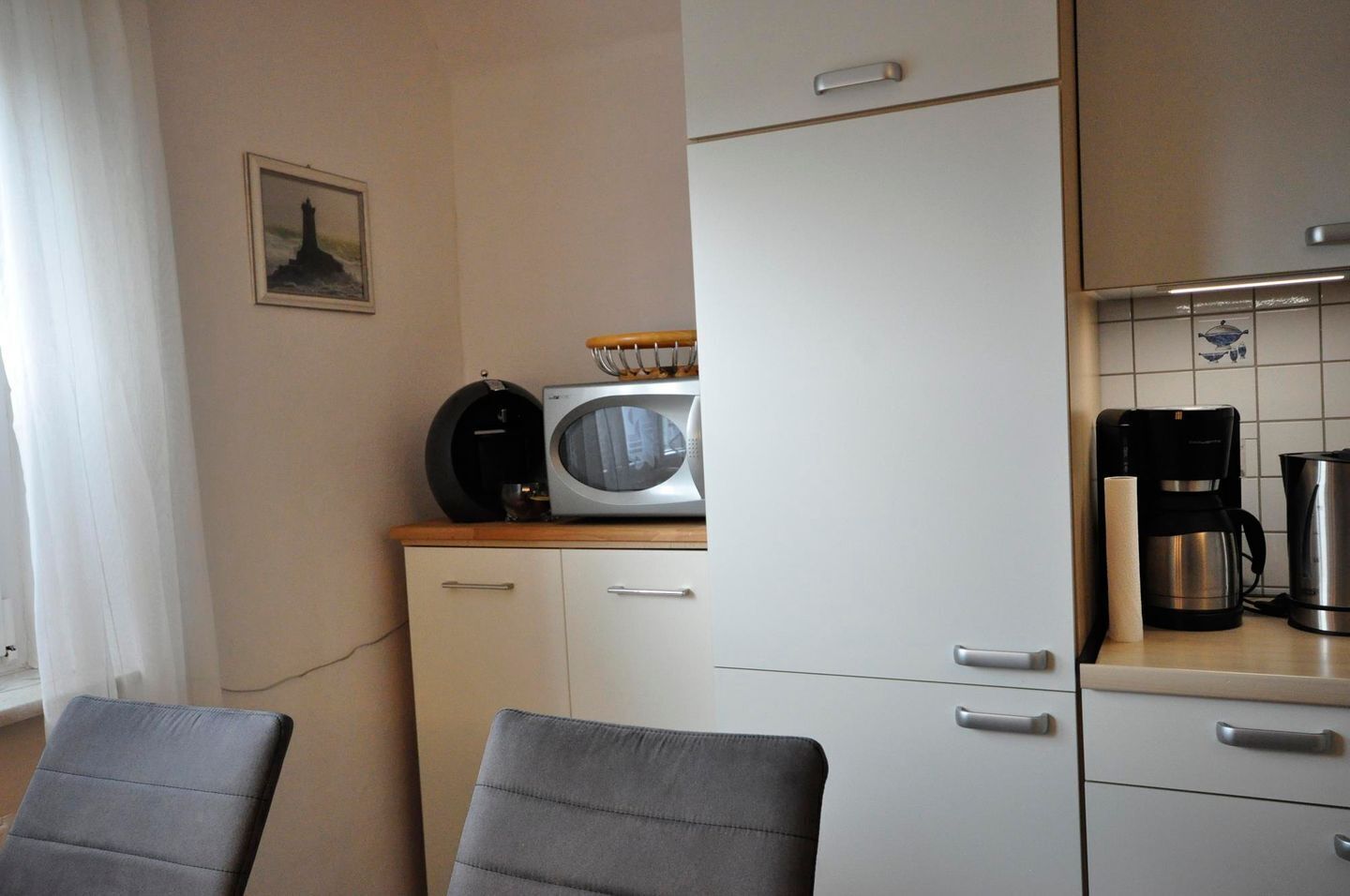 Une cuisine compacte  équipée d’un four à micro-ondes, d’une machine à café et d’un petit placard. On peut voir deux chaises au premier plan.