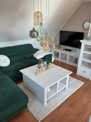 Uma sala de estar moderna com um sofá verde, uma mesa de centro branca e uma televisão.