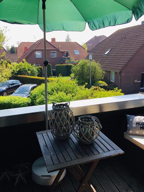 Un balcón con una mesa, dos faroles decorativos y un paraguas verde.
