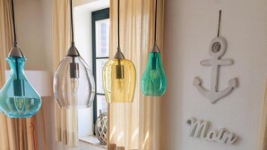 Un coin repas avec une table blanche, trois suspensions, un plaid en fausse fourrure et une décoration murale en forme d’ancre.
