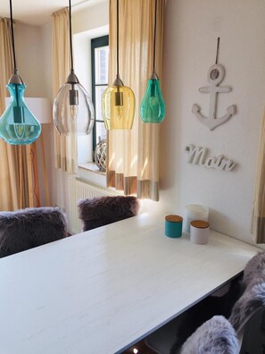 A dining area with a white table, three pendant lights, a fur throw, and a wall-mounted anchor decoration. - Vacation apartment Fischerstraße 1 (Wittmund)
