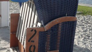 Une chaise en osier placée sur une plage de sable, avec le numéro « 2292 » inscrit dessus, et l’océan en arrière-plan.