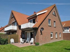 Ein zweistöckiges Backsteingebäude mit geneigtem Dach, einem Balkon und einer kleinen Terrasse mit Gartenmöbeln.