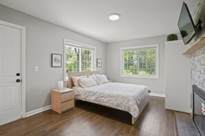 Quarto com cama, mesa de cabeceira e cômoda, janelas amplas e lareira.