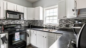 A kitchen with white cabinets, a black stove, a microwave, and a window. - Central Charm: 5min to Broadway & DT, Free Coffee! (Nashville)