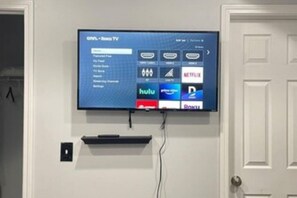 A flat-screen TV mounted on a wall with a menu interface displaying various streaming services.