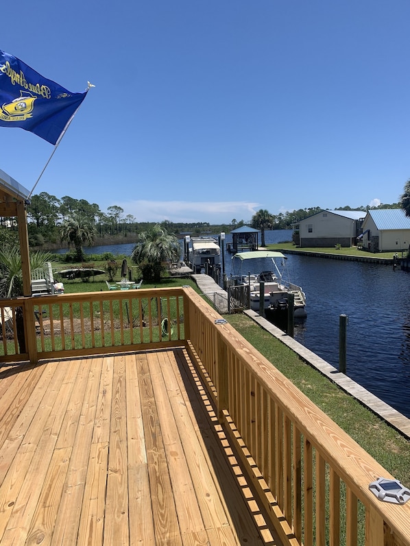 A wooden deck with a view of a marina, docked boats, and a house with a blue roof.