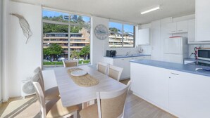 A modern kitchen with white cabinets, a blue countertop, and a dining area with a table and chairs. - Seaview 7 - Prime Position Beachside Holiday (AVOCA BEACH)