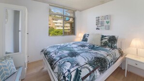 A bedroom with a bed, a nightstand, a window with a view, and a door. - Seaview 7 - Prime Position Beachside Holiday (AVOCA BEACH)