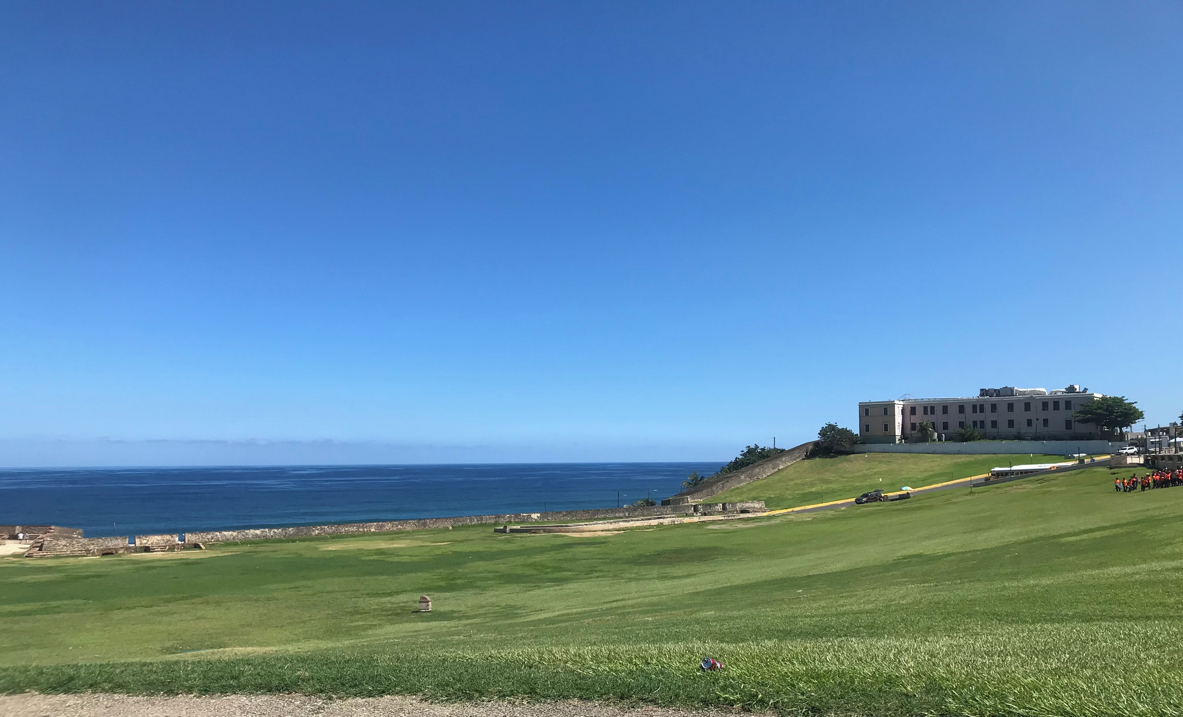 A coastal view with a grassy area, a building with multiple windows, and a clear blue sky.