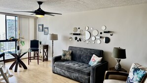 Una sala de estar moderna con un sofá gris, una mesa de comedor y un ventilador de techo.