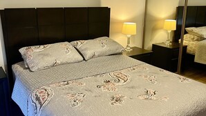 Una cama bien hecha con una colcha estampada, dos lámparas de noche y un espejo grande en la pared.